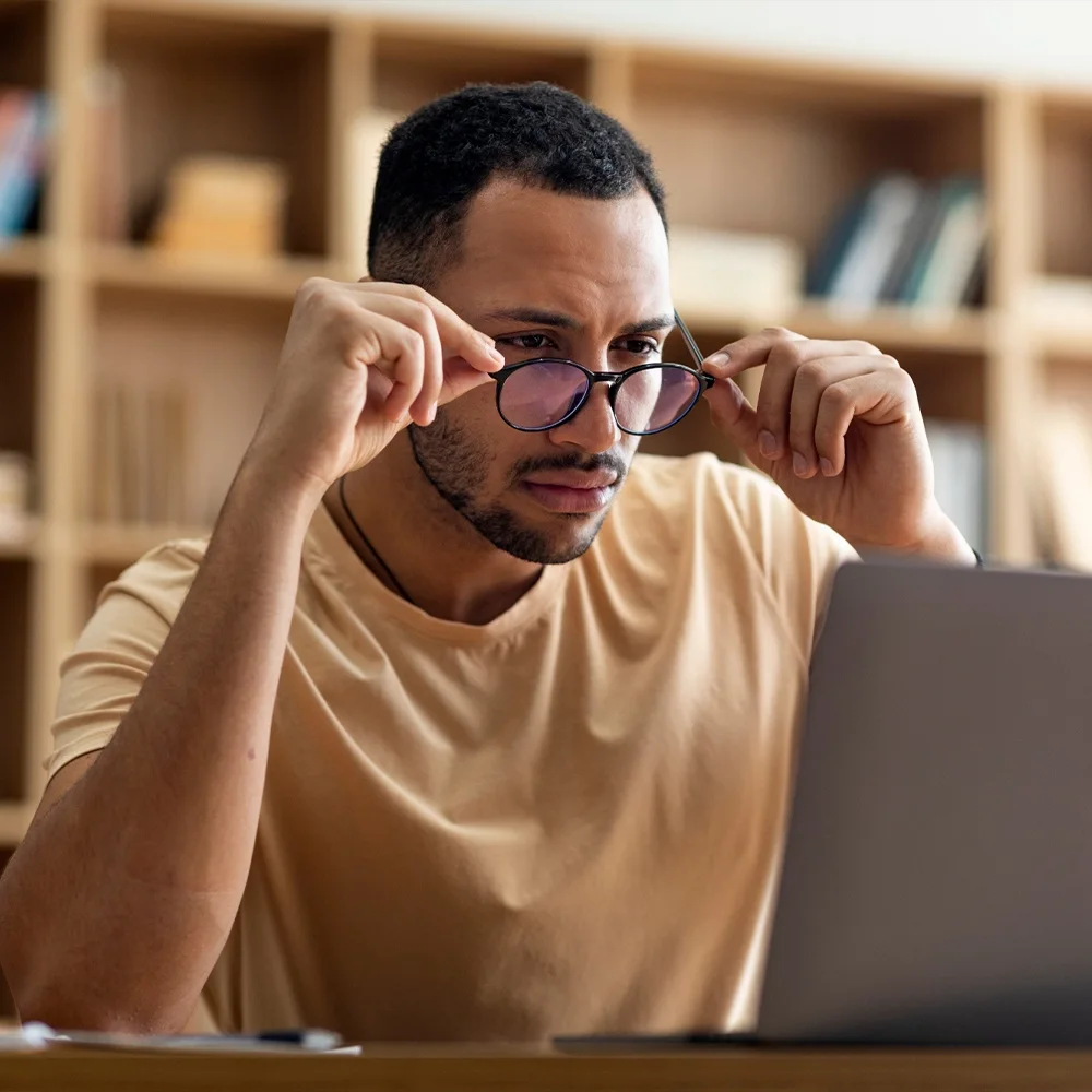 A man in glasses concentrating at a laptop in the late afternoon